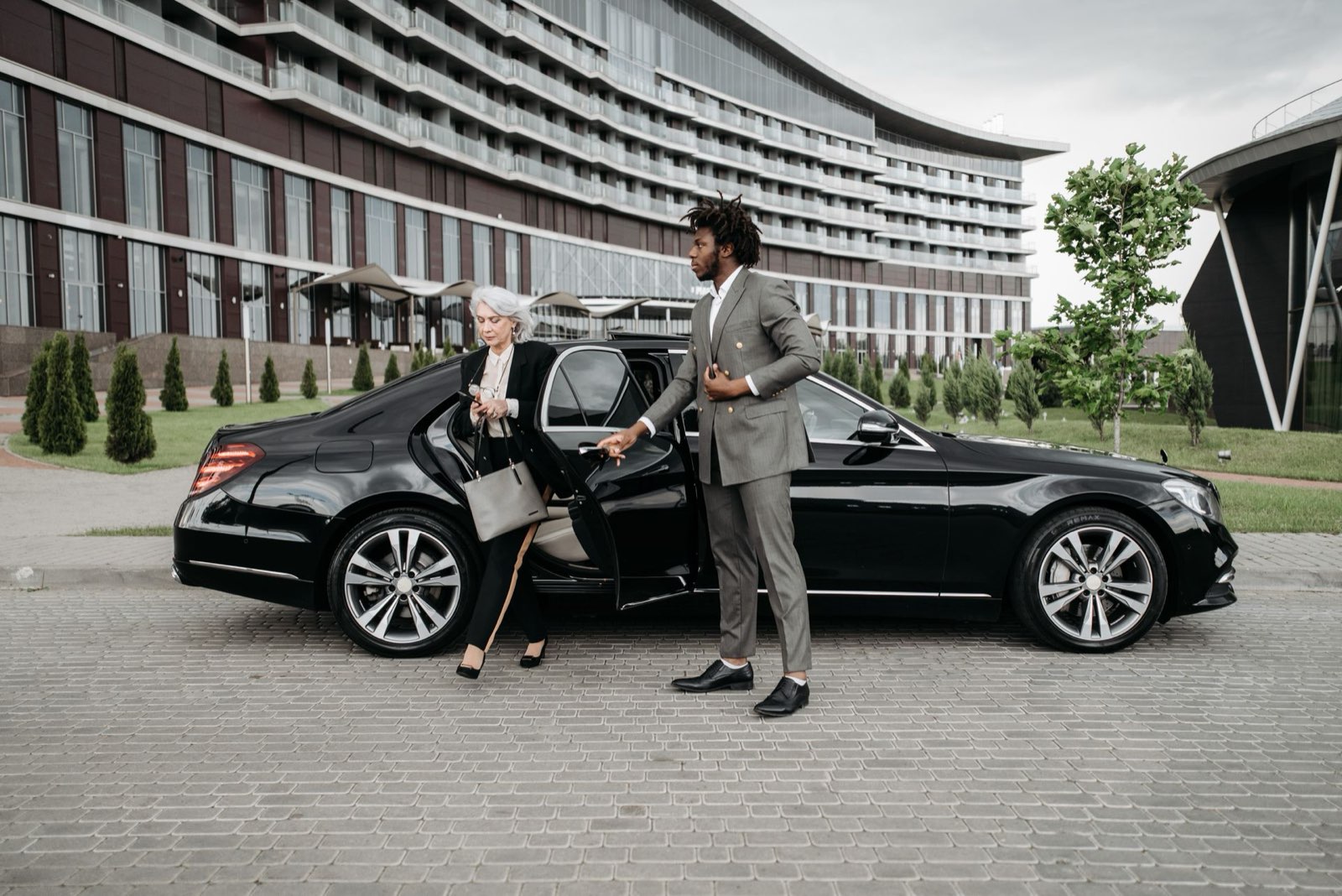 Chauffeur holding the rear door of a black Mercedes sedan open for a businesswoman